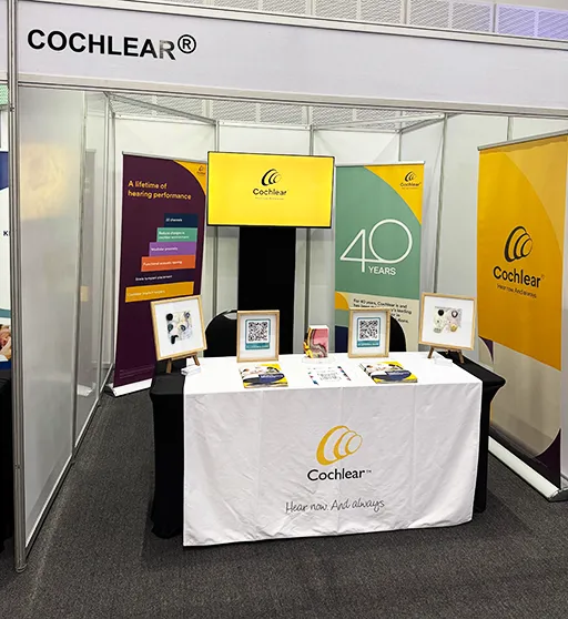 A booth at an expo for Cochlea, a medical device company. The booth, features a table covered in a tablecloth as well as pull-up banners printed by Brand Monster.